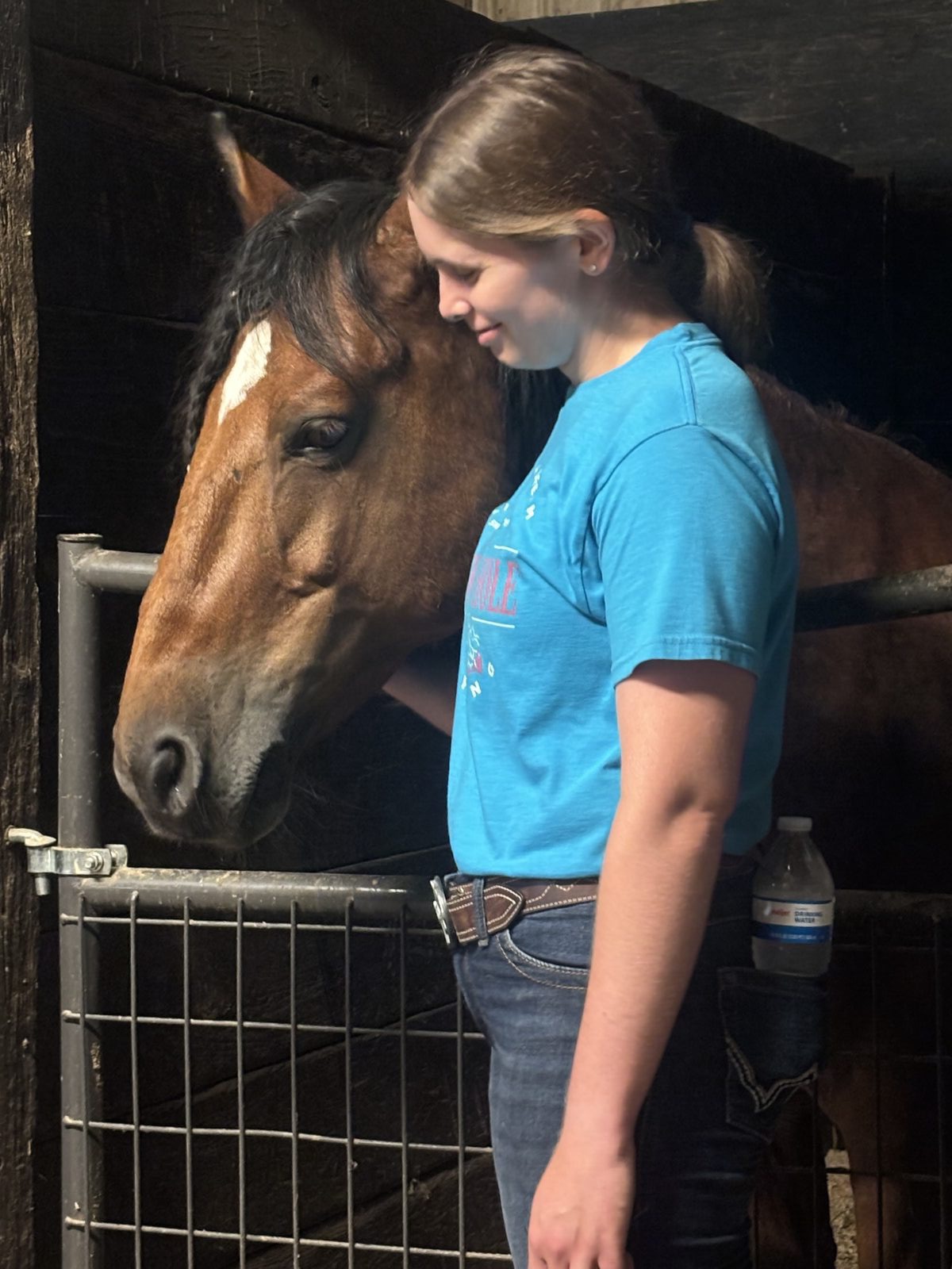 A young woman resting her head against a bay wild horse in its stall