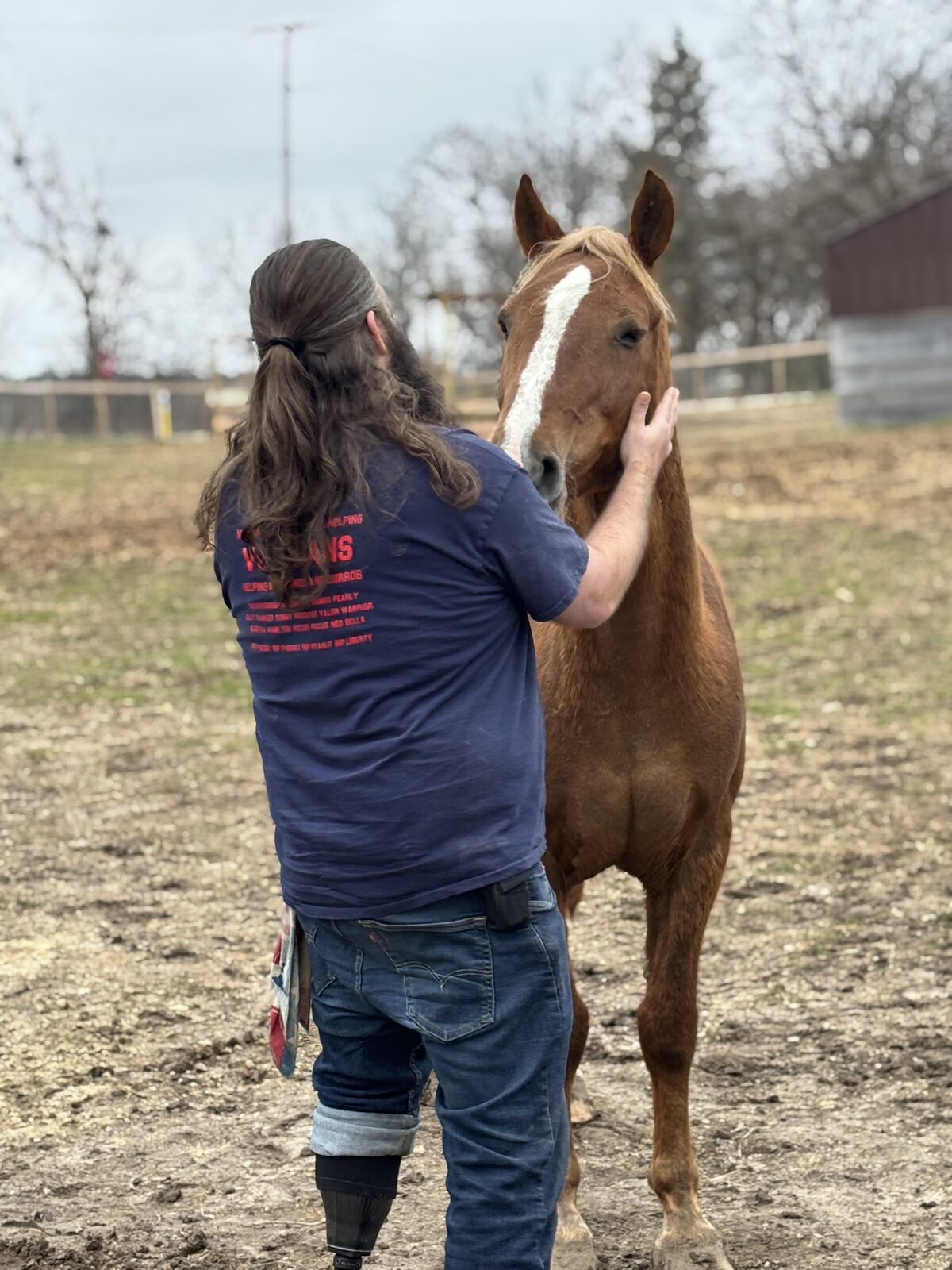 A veteran with a prosthetic leg resting his hand on a wild horse's face